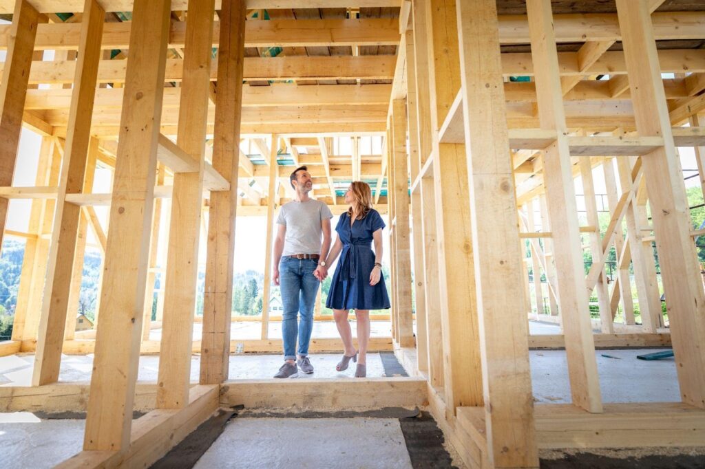 A couple standing in a partially built house, surrounded by construction materials