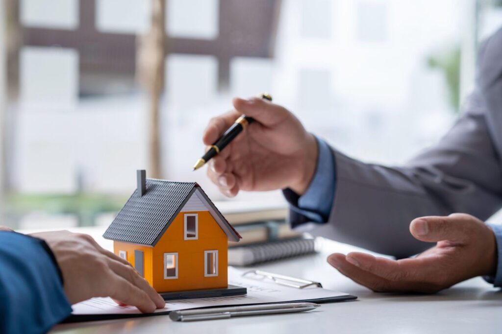 Two people signing a contract with a miniature house model, symbolizing a real estate deal