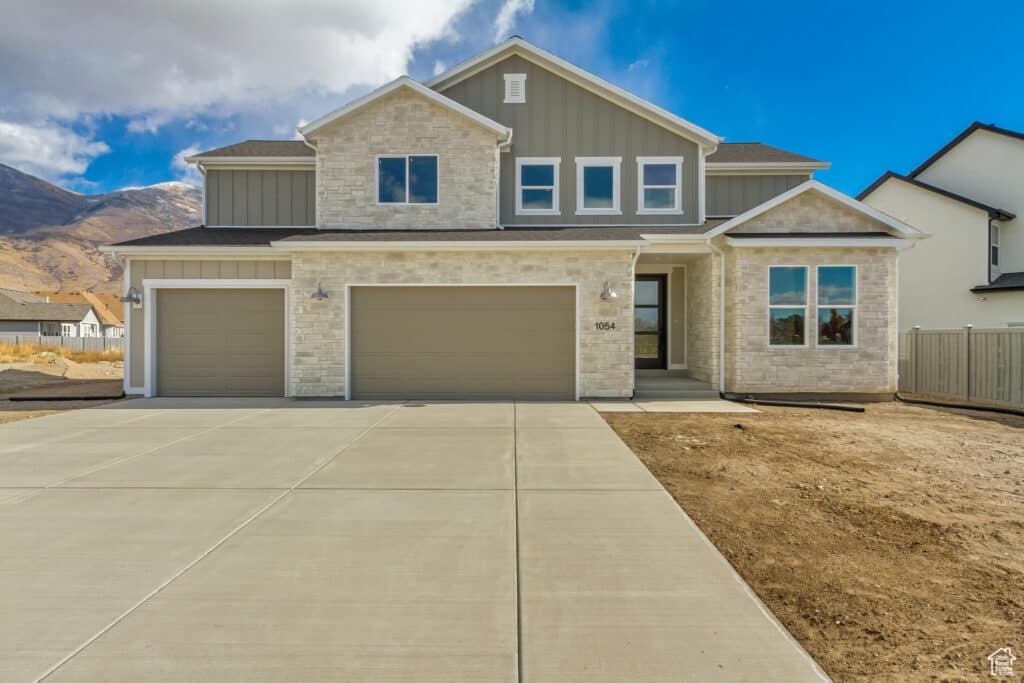 A charming residence featuring a driveway and garage, nestled in front of majestic mountains.