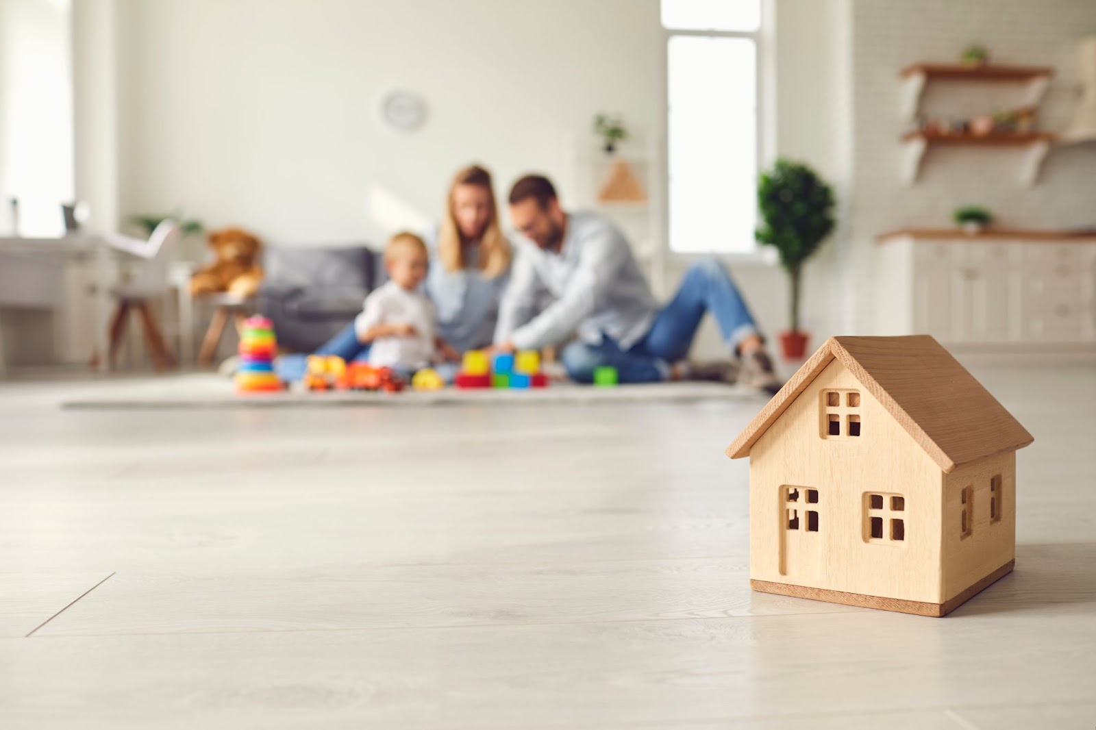 A family gathers in a cozy living room, enjoying time together near a colorful toy house on the floor.