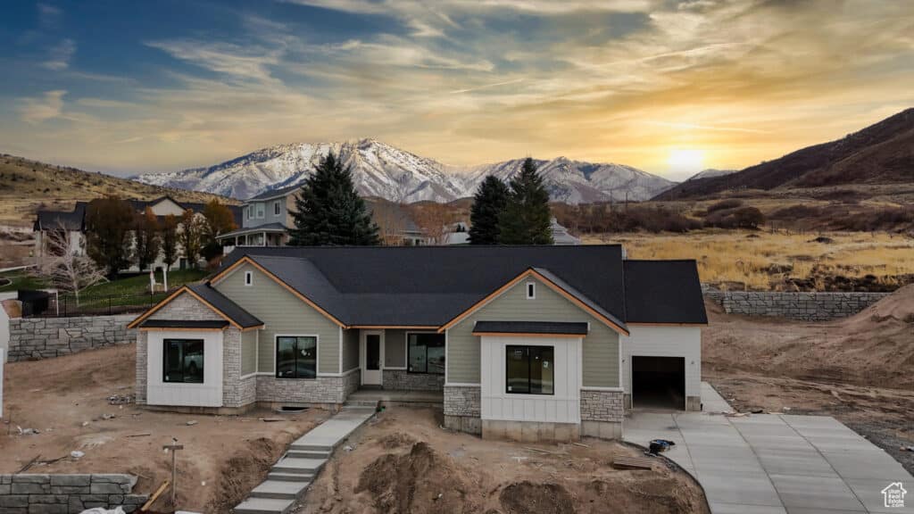 A house under construction with scaffolding, set against a backdrop of majestic mountains and a clear blue sky.