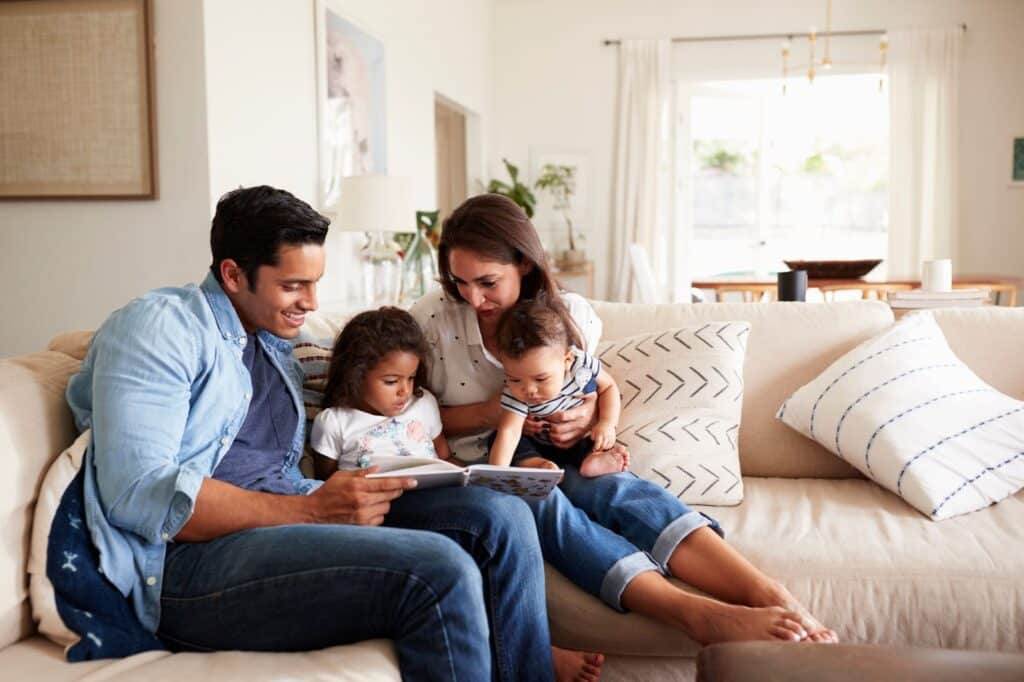 A family gathered on a couch, engrossed in reading a book together in their cozy, family-centric living room.