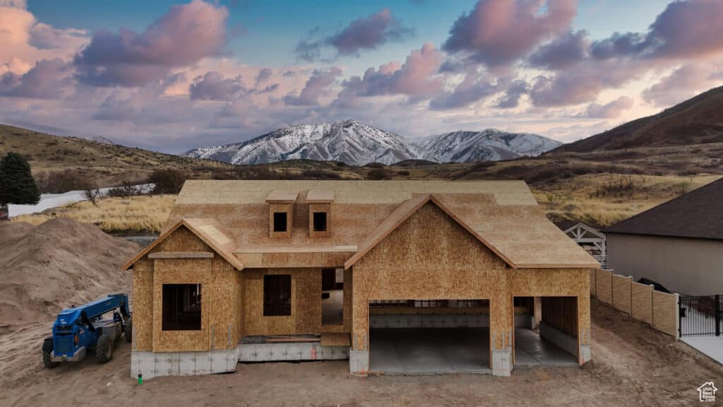 A construction site featuring a house in progress, framed by scenic mountains under a bright, sunny sky.